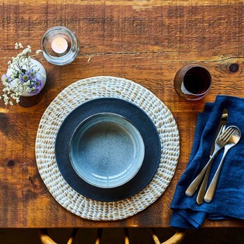 Bol et assiette posés sur un napperon rond, accompagnés d'un verre de vin, d'une bougie et d'un petit bouquet de fleurs.