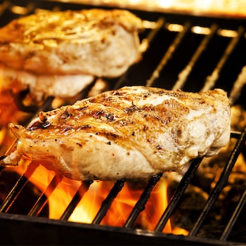 Deux poitrines de poulets qui grillent sur le BBQ avec des flammes.