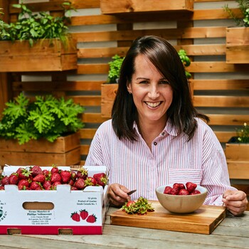 Geneviève O'Gleman est assise sur à une table à l'extérieur et elle équeute des fraises.
