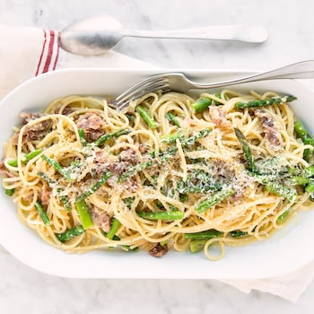 Du spaghetti carbonara aux asperges et au prosciutto dans une assiette de service.