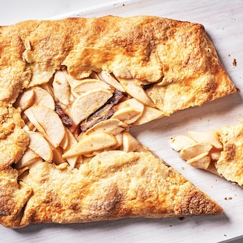 Une tarte rustique aux pommes, aux poires et aux dattes dans une assiette avec une part déjà coupée.
