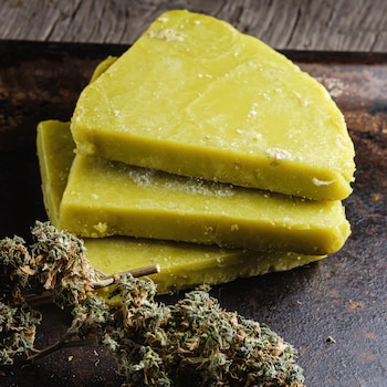 Trois morceaux de beurre de cannabis empilés les uns sur les autres à côté de têtes de cannabis.