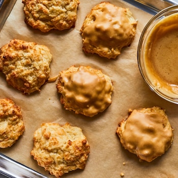 Des biscuits au cheddar et à l’érable sur une plaque de cuisson avec un bol de glaçage.
