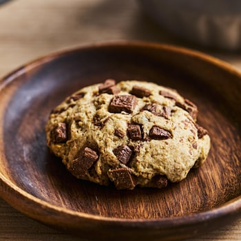 Un biscuit aux brisures de chocolat dans une assiette de bois.