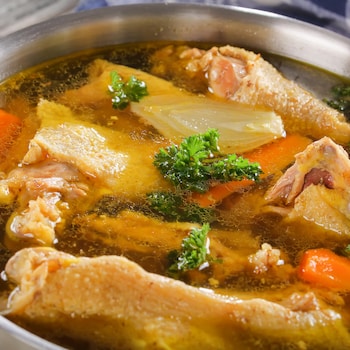 Une casserole remplie de morceaux de carcasse de poulet, de carottes, d'oignons et d'herbes fraîches.