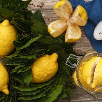 Des citrons et des feuilles de laurier sur un comptoir. À leurs côtés se trouve un pot en verre contenant des citrons et du sel.