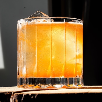 Un cocktail orangé avec de la glace sur une bûche du bois.
