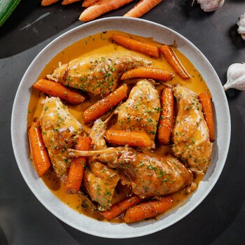 Un bol avec des cuisses de lapin et des carottes. 