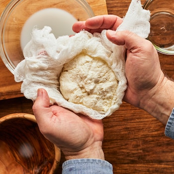 Deux mains tiennent une boule de fromage ricotta fait maison à la main. 