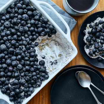 Un plat de service rempli de gâteau-frigo aux bleuets, avec une assiette servie, une théière et une tasse de thé à côté. 