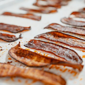 Plusieurs tranches de bacon végétalien à l'aubergine sur du papier parchemin. 