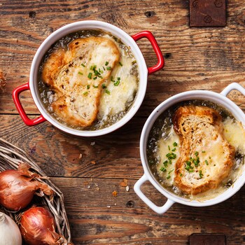 Deux bols de soupe à l'oignon recouverts d'un croûton de pain et de fromage fondu sur une planche de bois, vus de haut.