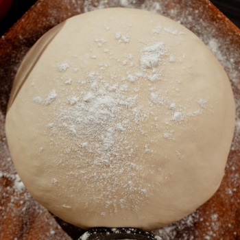 Un boule de pâte recouverte de farine dans une assiette en bois.