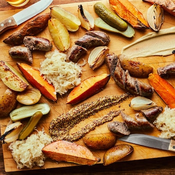 Il est possible de voir, sur une planche de bois, des saucisses, légumes rôtis, cornichons et choucroute.