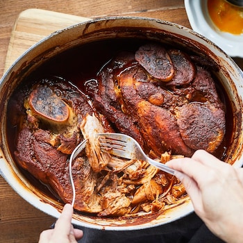 Mains en train d'effilocher le porc cuit qui se trouve dans un grand plat à cuisson. 