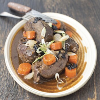 Des gros morceaux de viande cuite, des morceaux de carotte et des rondelles d'oignon dans un bouillon, dans une assiette.