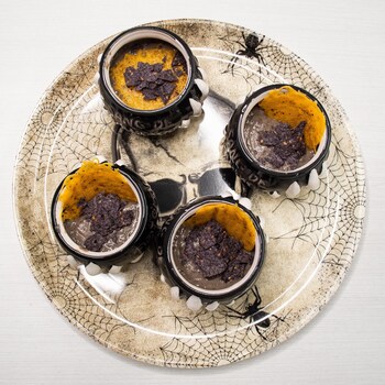 Quatre petits pots en forme de chaudron de sorcière remplis de potage aux haricots noir et à la bière dans une assiette au thème de l'Halloween.
