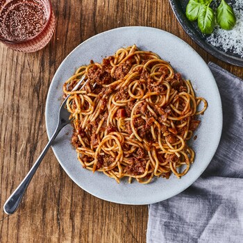 Une assiette de spaghetti avec un verre d’eau pétillante et un bol de parmesan. 