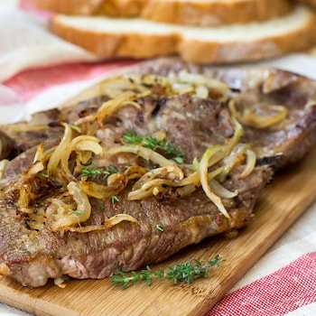 Une steak sur une planche de bois et des oignons frits.
