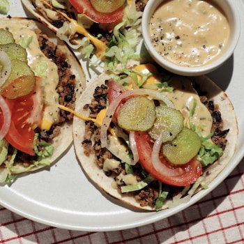 Trois tacos végétaliens dans une assiette avec un petit bol de sauce.