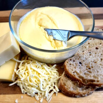 Un bol avec de la trempette au fromage avec des croûtons de pain et des morceaux de fromages.