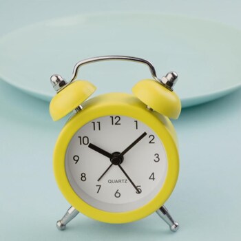 Une horloge jaune devant une assiette vide.