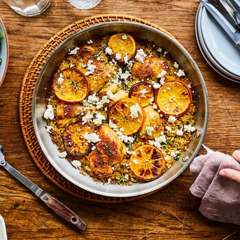 Un poulet grillé repose sur un lit de riz, garni d'oranges également grillées dans un poêlon.