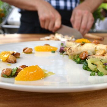 Pieuvre grillée et salade estivale avec des suprêmes d'orange dans une assiette blanche.