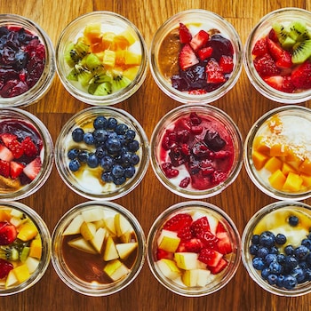 Douze pots en verre, remplis de yogourt garni d'une variété de fruits, sont disposés symétriquement sur une table.
