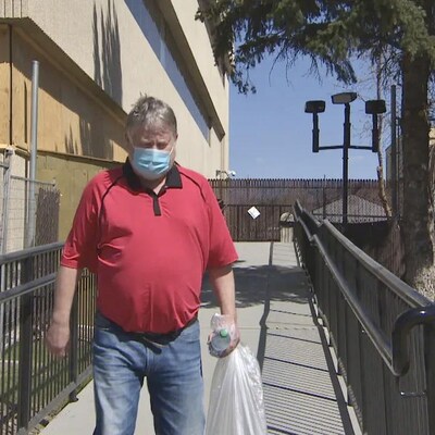 Un homme tient un sac et une bouteille dans la main et porte un masque.