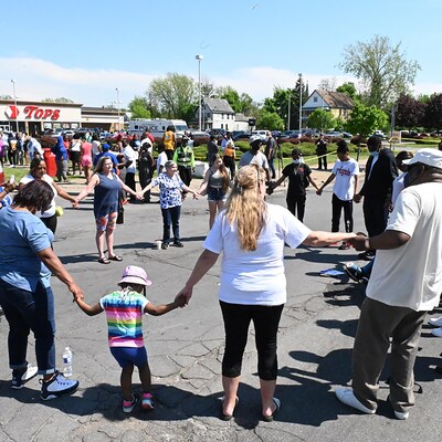 Des gens forment un cercle en se tenant les mains à un coin de rue adjacent à un supermarché où a eu lieu une tuerie. 