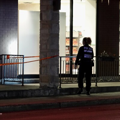 Une policière inspecte la façade du commerce avec sa lampe torche.                        