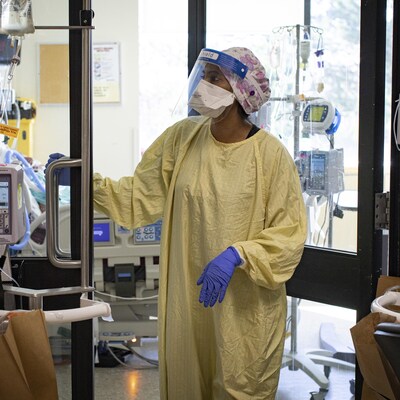 Une infirmière portant un masque, une visière et une tenue protectrice contre la COVID-19 sort de la chambre d'un patient aux soins intensifs.