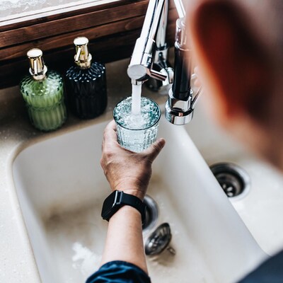 Un homme remplit un verre d'eau au robinet d'une cuisine.