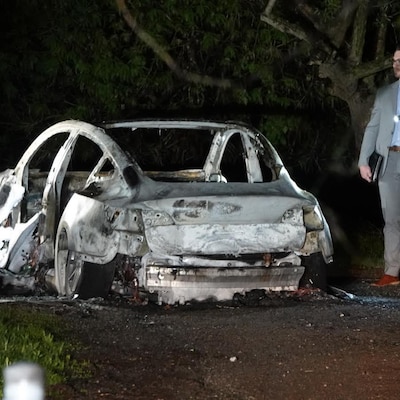 Des enquêteurs pointent leur lampe de poche vers la carcasse du véhicule incendié la nuit.