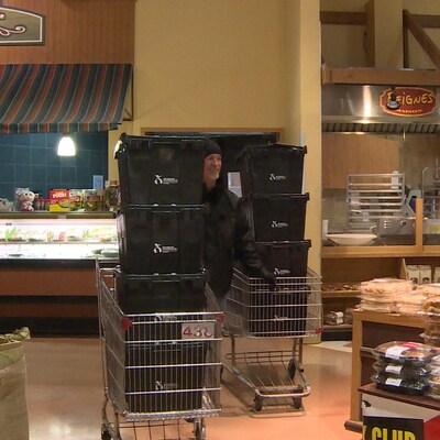 Un homme entre deux paniers d'épiceries remplis de caisses noires dans un supermarché. 