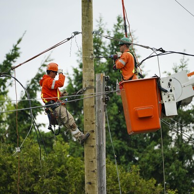 Deux travailleurs Hydro-Québec réparent un poteau électrique.
