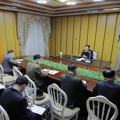 Kim Jong-un, assis à un bureau, s'adresse à des hommes qui sont assis devant lui en prenant des notes.