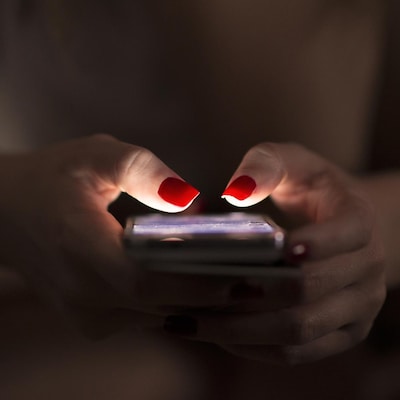 Un gros plan sur les mains d'une femme tenant un téléphone intelligent. Les ongles rouges de la femme sont éclairés par l'écran.