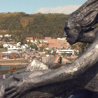 Un bronze d'une femme et d'un poison en avant plan de la ville de Gaspé.