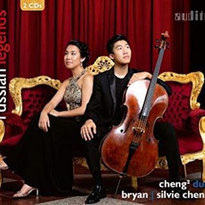 2 musiciens, 1 jeune homme et une jeune femme d'origine asiatique, assis en tenue de soirée sur un fauteuil de style baroque, rouge et or.