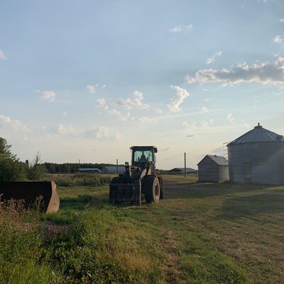 L'arrière court d’une ferme, un tracteur au centre de l'image et de petits silos à grains sur la droite. 