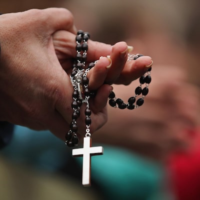 Les mains jointes, une paroissienne tient un chapelet avec une croix bien visible au bout de la chaîne.
