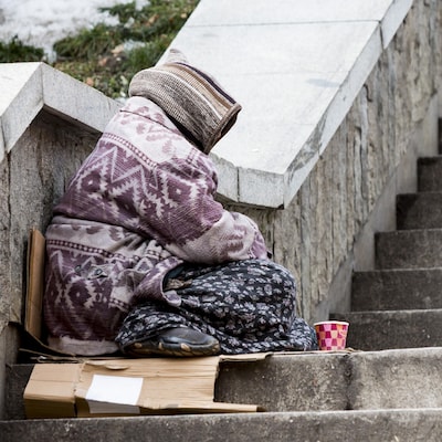 Profil d'une femme emmitouflée dans ses vêtements et assise dans un escalier.