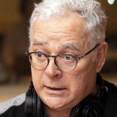 Un homme portant des lunettes parle devant un micro.