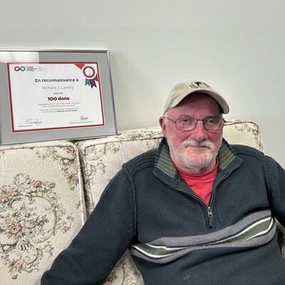 Richard Landry assit sur un canapé avec le certificat qu'il a reçu de la Société canadienne du sang.