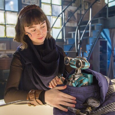 Elle regarde tendrement le robot et dépose sa main sur lui. 