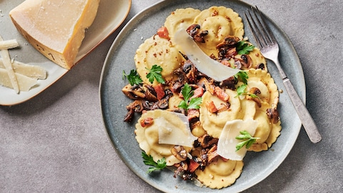 Des raviolis avec une sauce aux champignons et à la pancetta dans une assiette.
