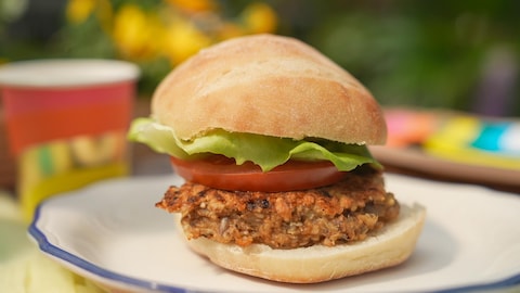 Une boulette d'avoine servie dans un pain à hamburger avec une tranche de tomate et une feuille de laitue.