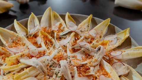 Des endives dans une assiette avec des anchois, des radis et de la chapelure épicée